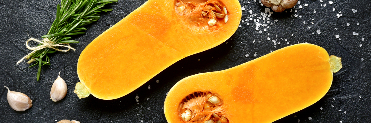 Halves of raw organic butternut squash with spices and ingredients for cooking.