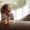 A young girl sitting on a couch, looking up.