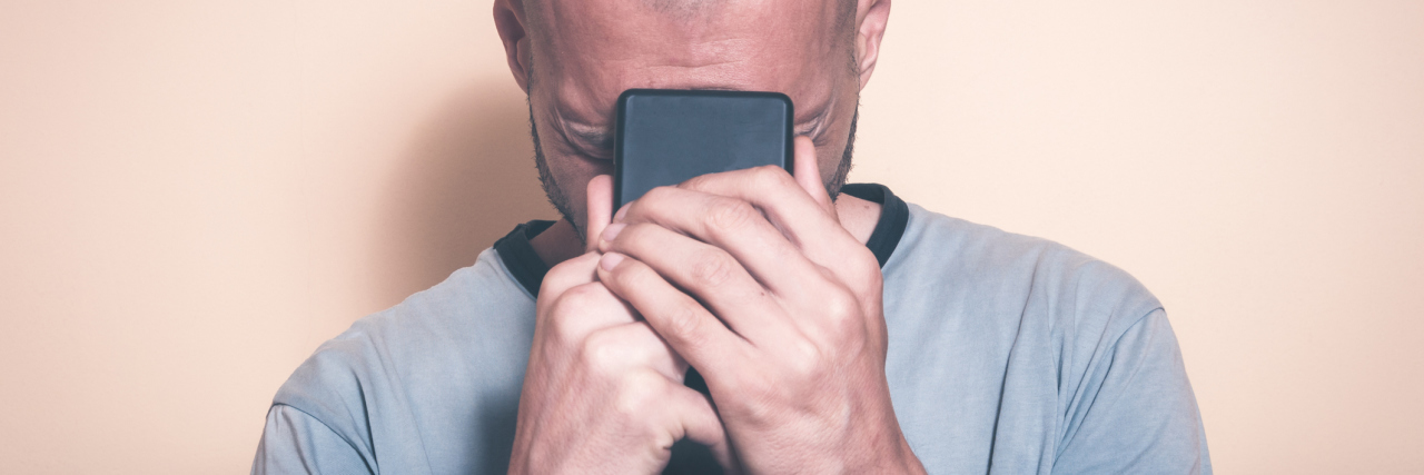 photo of man holding phone in hands and close to face, crying