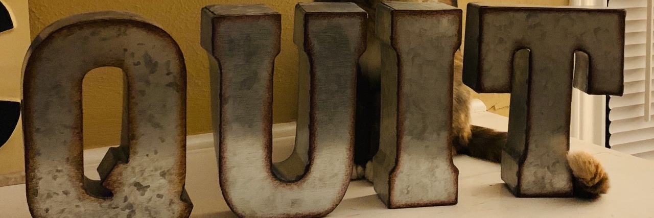 Quitting Doesn't Mean Failure in My Life With a Disability Letters on shelf spelling "Quit" with a yawning cat in the background.
