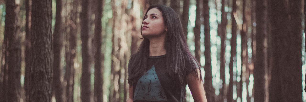 photo of woman in woods looking contemplative up at sky or trees