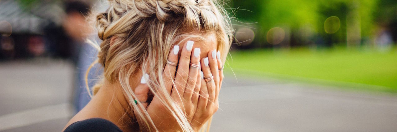 What It's Like Living With Anxiety A woman with blonde hair covering her face with her hands
