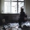 photo of woman holding rose and sitting on hair in abandoned room with papers all around floor