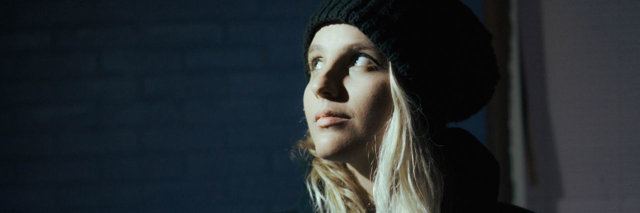 Why I'm Grateful for My Depression photo of woman looking up at light in darkness with dark hoodie and smile on face