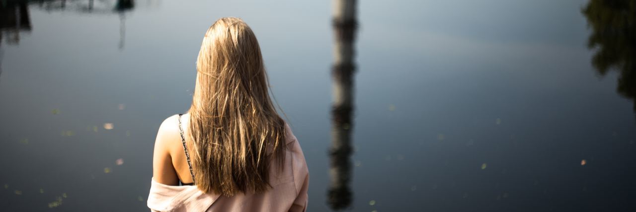 What Life Is Like With an Eating Disorder Nobody Seems to Know photo of young woman with blonde hair sitting in front of water with reflection of tall spire or tower