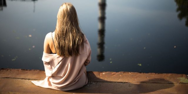 What Life Is Like With an Eating Disorder Nobody Seems to Know photo of young woman with blonde hair sitting in front of water with reflection of tall spire or tower
