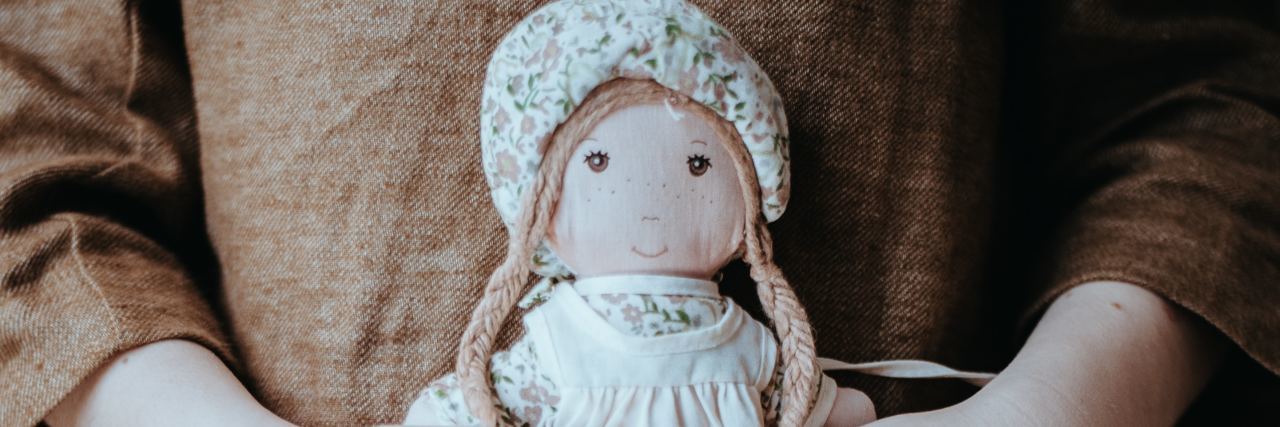 photo of young girl with hamsas on hands holding doll to her dress