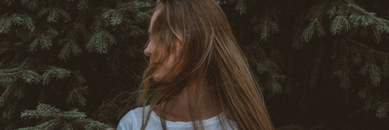 photo of woman standing in front of trees turned to side and hair hiding face