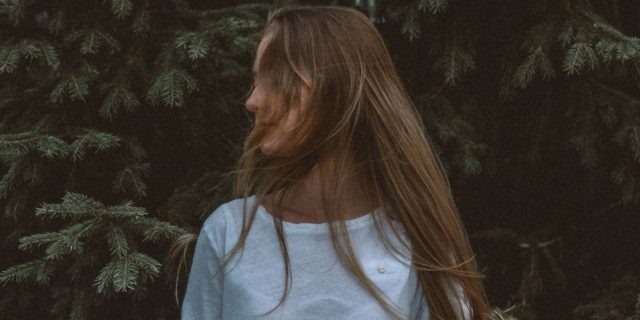 photo of woman standing in front of trees turned to side and hair hiding face
