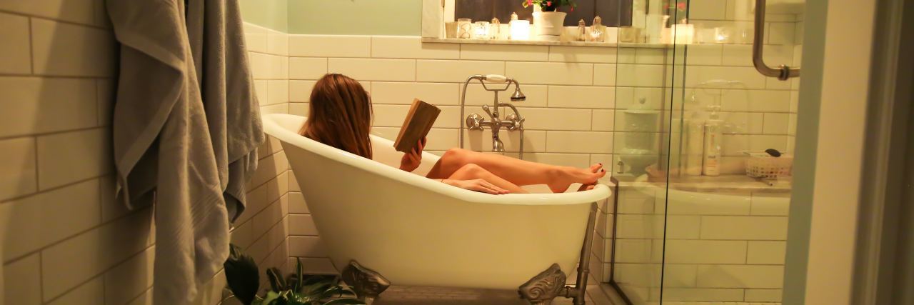 What Actually Is Self-Care? photo of woman in bath, reading a book, taken from afar