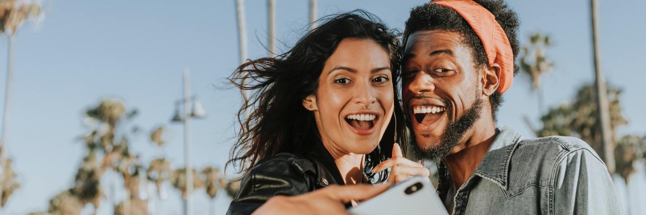 What Is a Friend, Anyway? two friends taking a selfie with palm trees in background