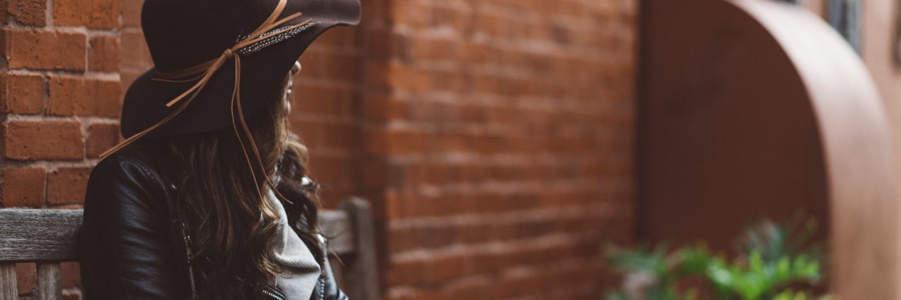 How to Control Anxious Thoughts photo of woman wearing hat and leather jacket sitting by brick wall and facing away from camera