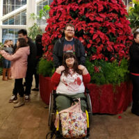 Jane with her boyfriend in front of a large poinsettia Christmas tree.