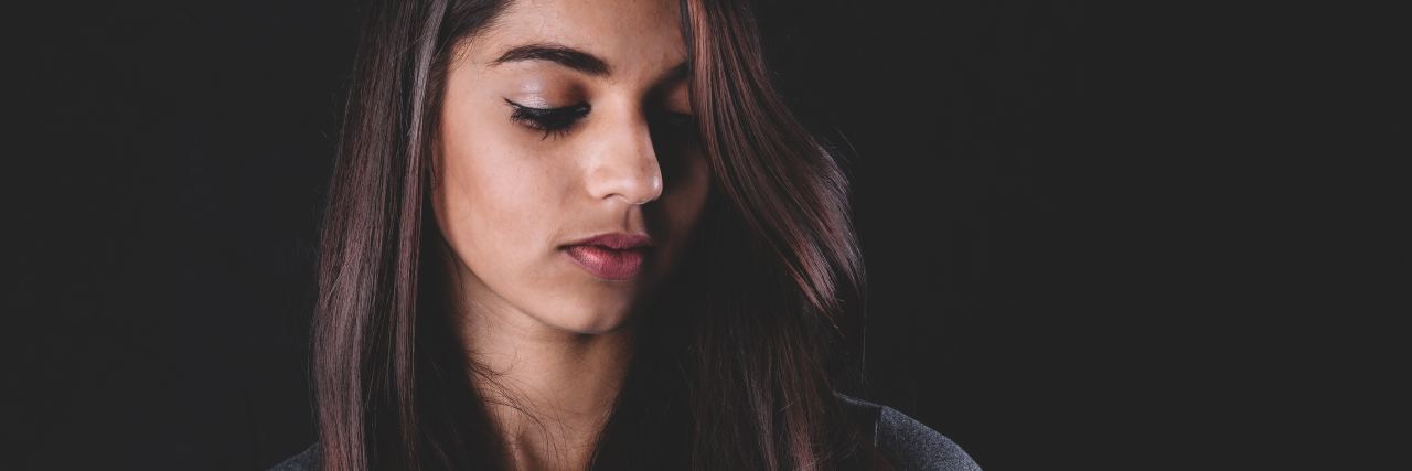 What to Know About Being an Introvert With Social Anxiety photo of woman against dark background with eyes closed and long brown hair