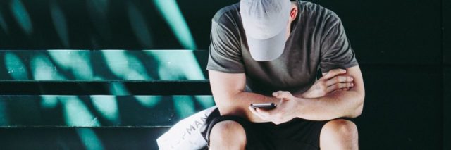 photo of man on bench in los angeles immersed in smartphone with cap covering face