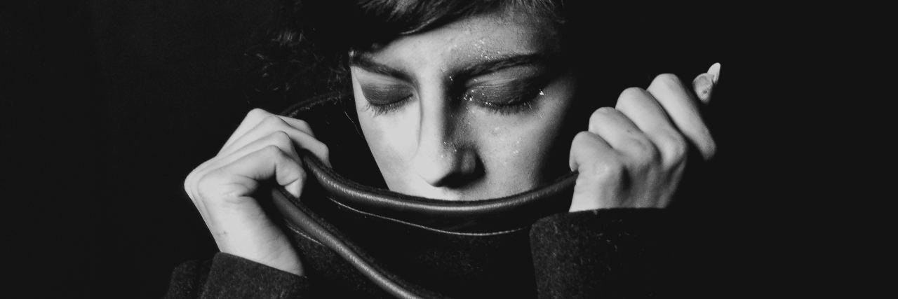 black and white photo of woman with eyes closed and pulling scarf up to cover her mouth