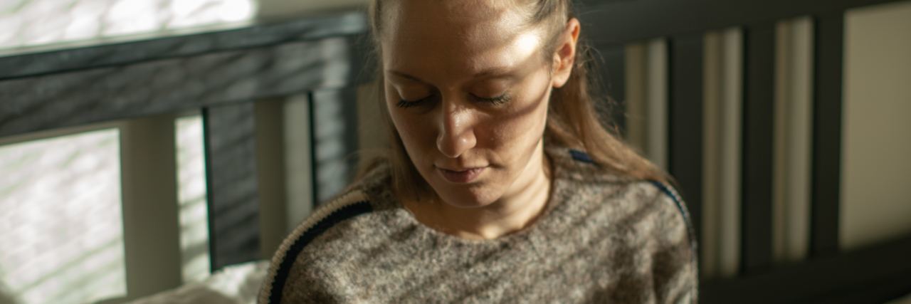 When Depression Is Triggered by Spring and Summer photo of woman sitting on bed with eyes closed in sadness and sun coming through window casting shadows onto her