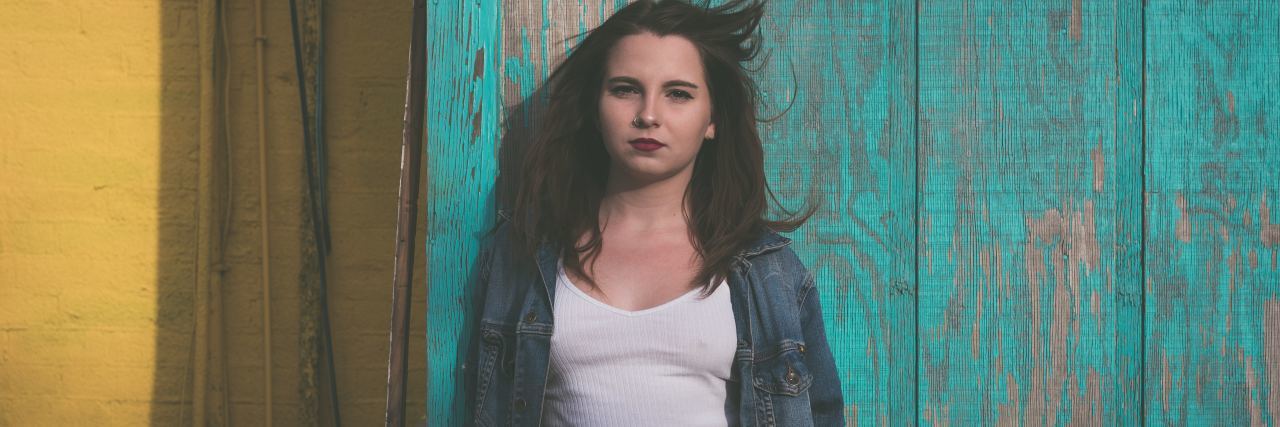 Responsibility to Talk About Youth Suicide After Sydney Aiello’s Death photo of young woman standing against blue wood panels looking serious into camera