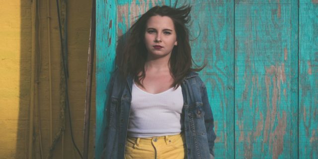 It’s Everyone’s Responsibility to Talk About Youth Suicide photo of young woman standing against blue wood panels looking serious into camera