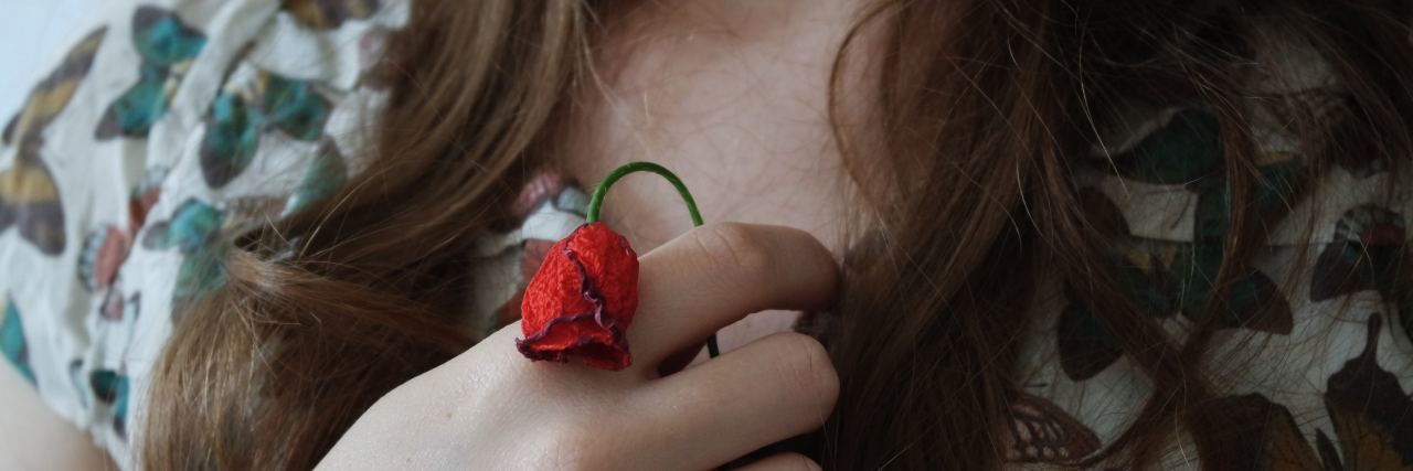 close up photo of woman holding small wilted rose close to chest
