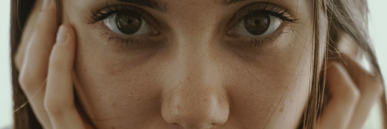 Why We Need to Stop Being Afraid of Talking About Suicide close up photo of young woman looking into camera with head resting on hands and serious face