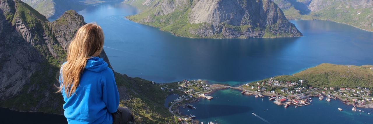 What to Know About Backpacking With Bipolar Disorder photo of young woman backpacking or traveling on top of mountain looking at mountains and lakes far below