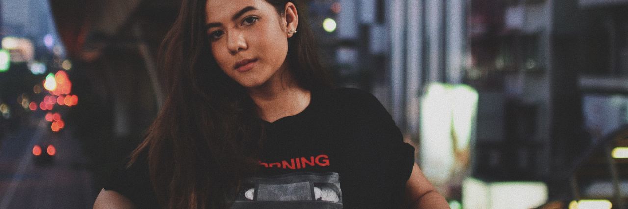 photo of young asian woman looking into camera on balcony over busy street