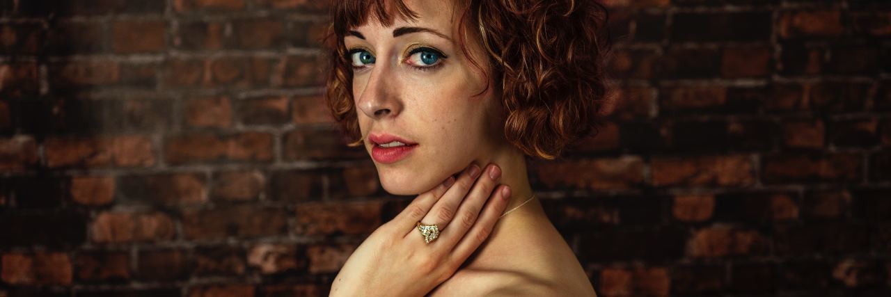 The Positive in Rebuilding Myself After a Bipolar Breakdown photo of woman standing in front of brick wall looking into camera and wearing green dress
