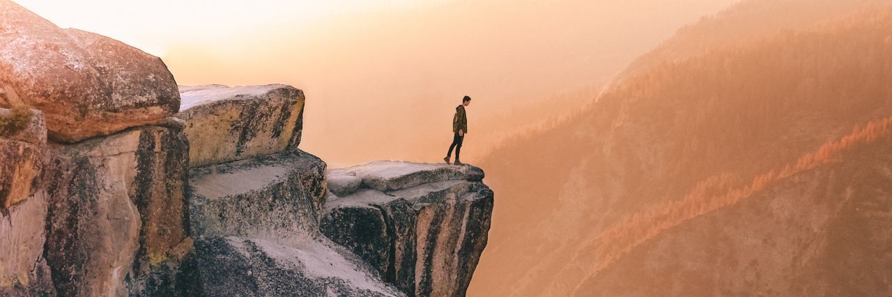 photo of man standing on cliff edge at sunset looking out over edge