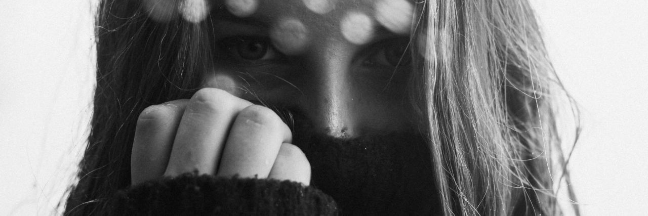 black and white close up photo of woman covering most of face with clothing and hand up to face, looking into camera with angry look