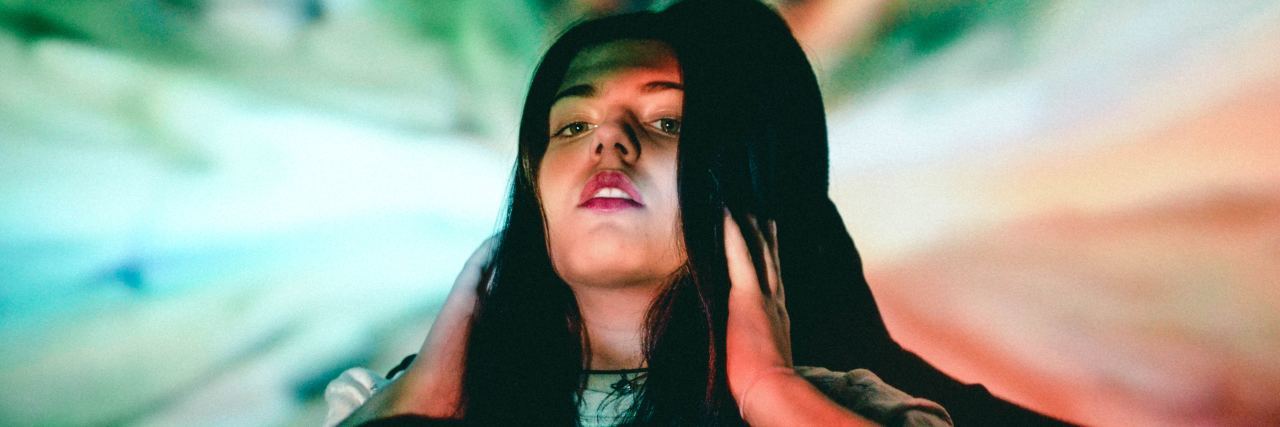 What Hypothyroidism Is and Is Not woman with dark hair sitting against a multicolored wall