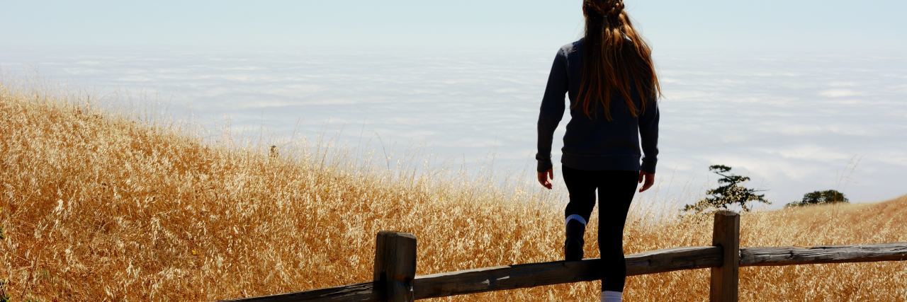 How to Commit to Therapy Borderline Personality Disorder photo of woman stepping over fence in orange wheat field with blue sky behind her