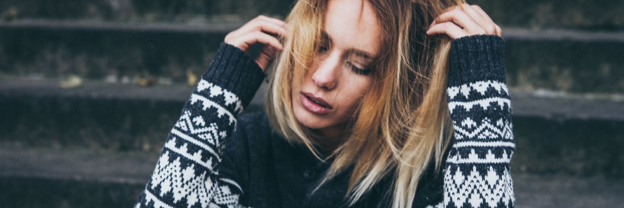 Finding It Hard to Move on After an Undiagnosed Illness photo of woman sitting on steps with eyes closed and hands in hair looking anxious