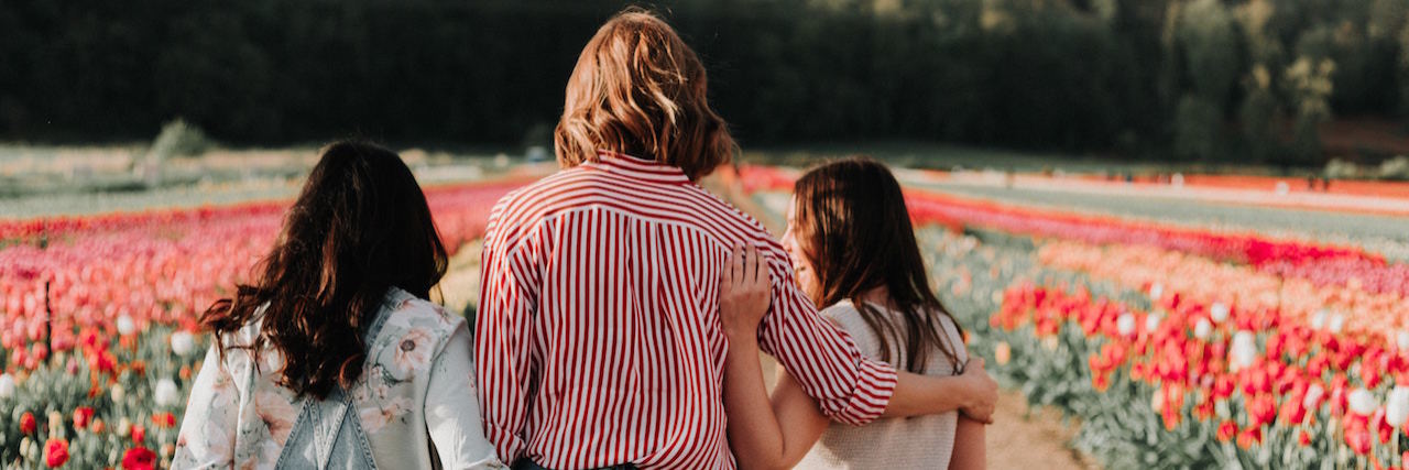 What to Know When Supporting Someone With Their Mental Health A group of friends facing away, arms around each other. They're standing in a field of flowers.
