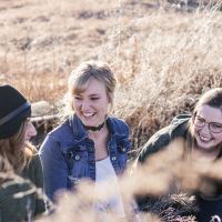 three friends smiling and talking with each other in a field