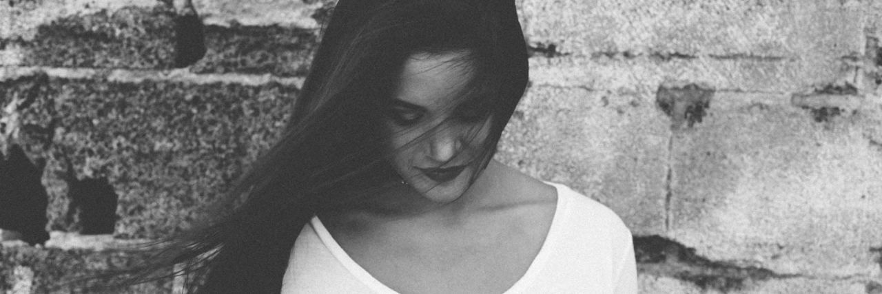 When You Stop Trying to Prove Your Chronic Illness to Others black and white photo of dark-haired woman against brick wall, who is looking down at her t-shirt which says believe in yourself
