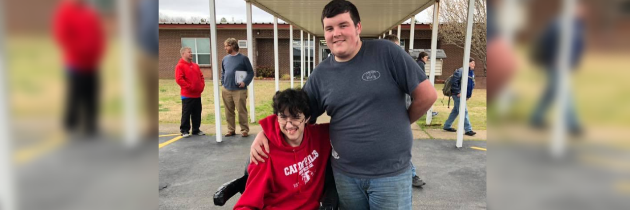 Tanner Wilson and his friend Brandon Qualls at their high school. Brandon is sitting in the wheelchair Tanner bought for him.
