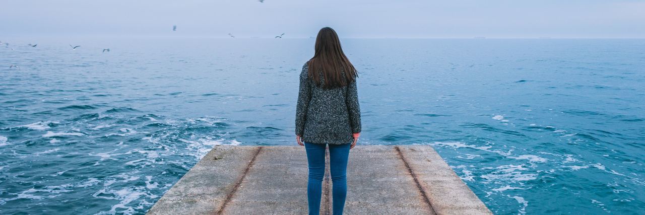 photo of woman standing on pier looking into distance over rough sea or lake at misty horizon