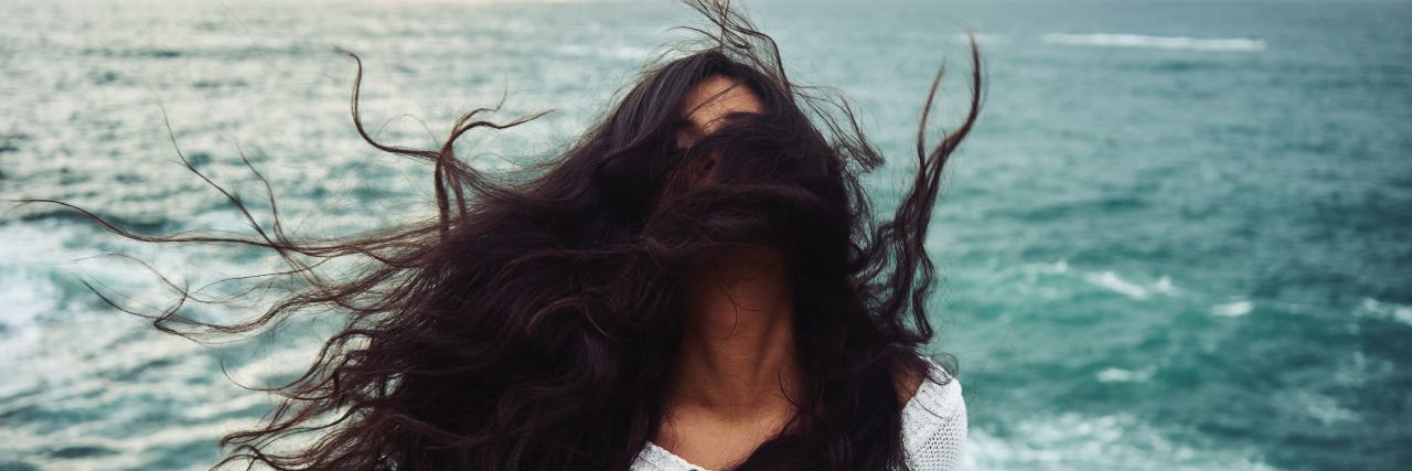 photo of woman in front of stormy sea throwing head back with windswept hair