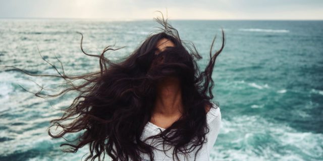 photo of woman in front of stormy sea throwing head back with windswept hair