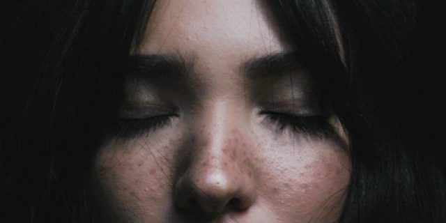 6 Myths (And Facts) About Schizophrenia You Really Need to Know close up photo of dark haired woman with eyes closed and hands raised to neck