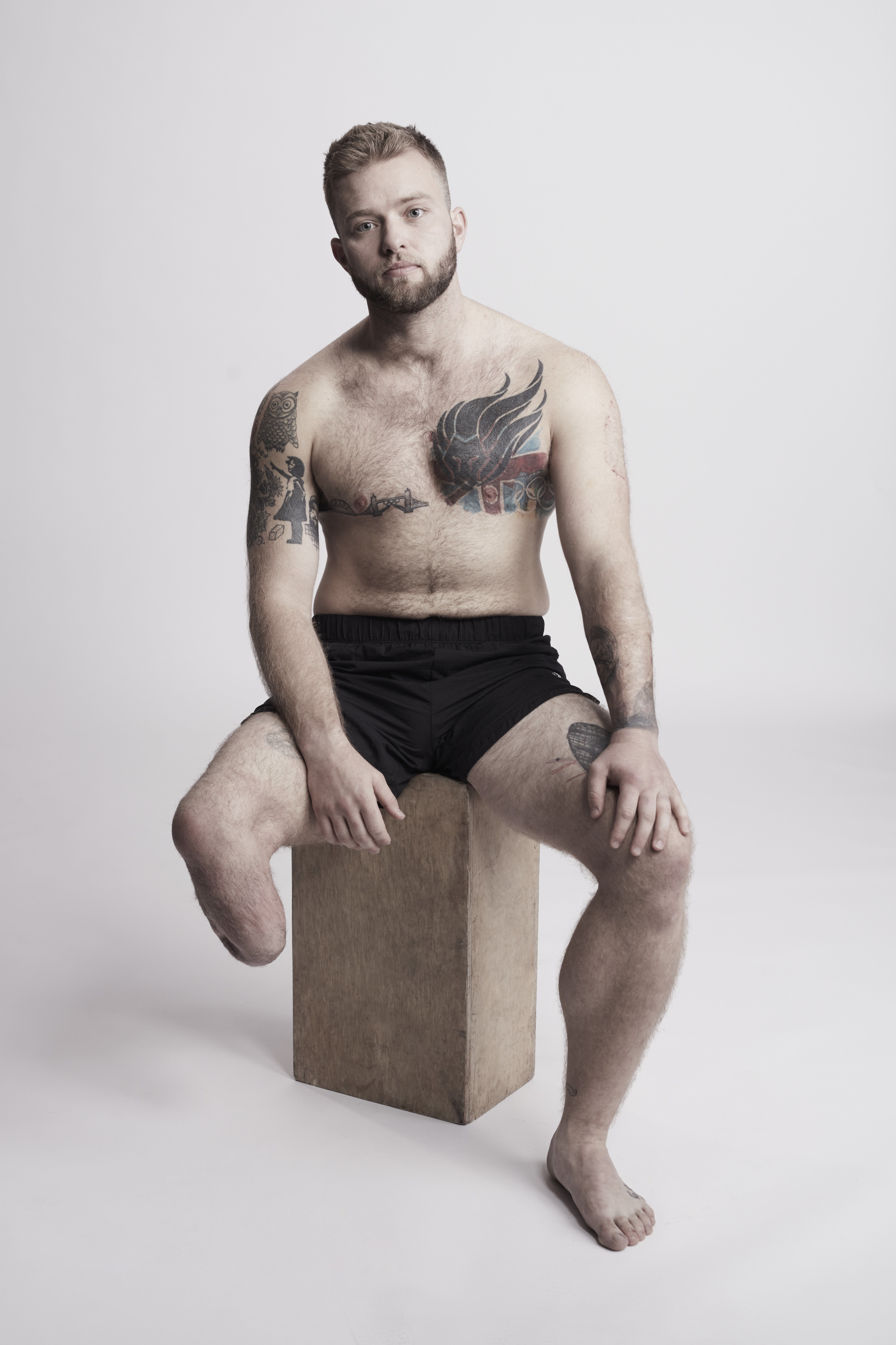 Jamie, a man with lower limb amputation and tattoos sitting on a wooden stool.