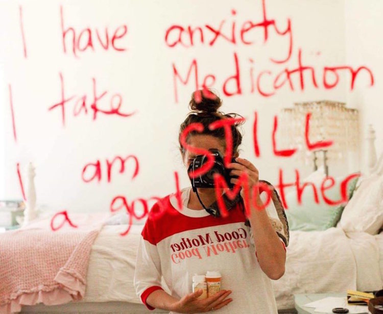 A woman holding pill bottles, taking a mirror selfie. The mirror shows the words: I have anxiety, I take medication and I am still a good mom