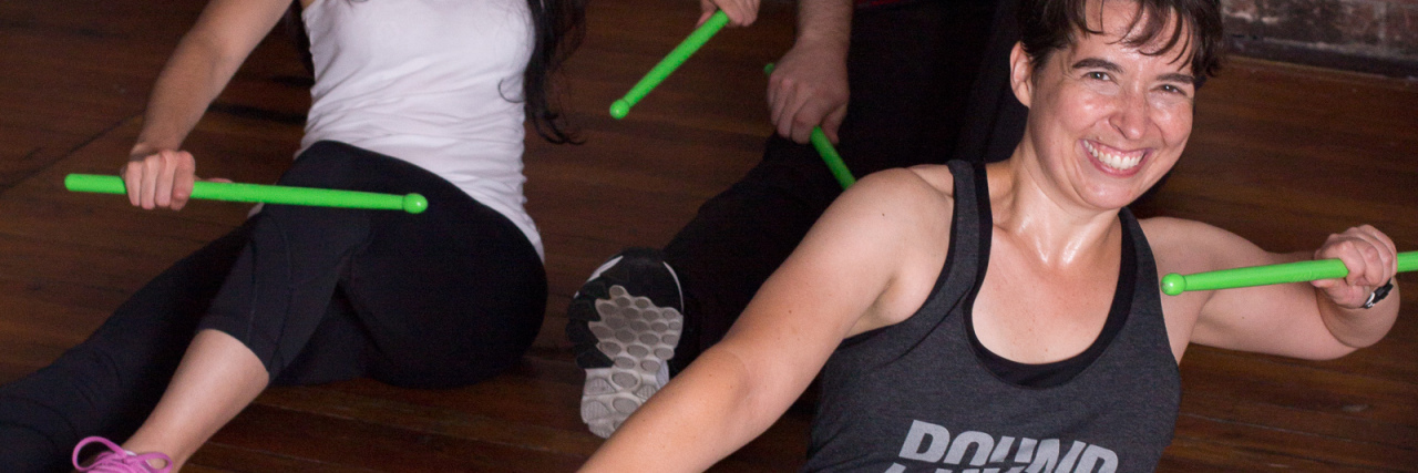 Exercise Techniques for Chronic Pain and Muscle Weakness Photo of contributor melissa hope posing in fitness class holding green sticks and smiling for camera