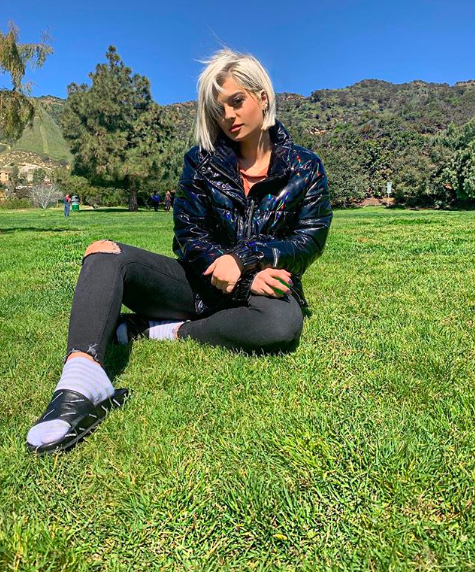 Bebe Rexha sitting on a lawn on a sunny day