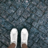 Girl in white sneakers is standing on paving stones