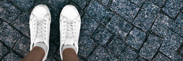 Girl in white sneakers is standing on paving stones