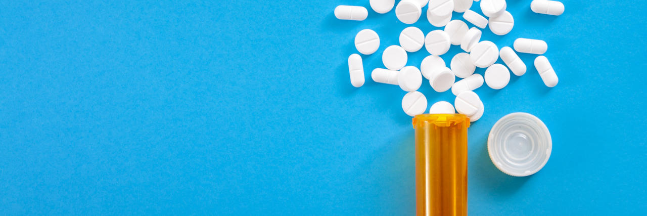 Pills falling from pill bottle on blue background