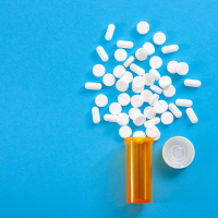 Pills falling from pill bottle on blue background