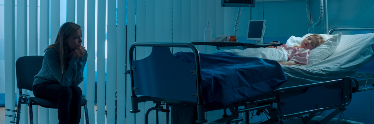 The Struggles of Parenting a Child With Epilepsy Child in hospital bed with mother sitting on a child watching her child, worried.